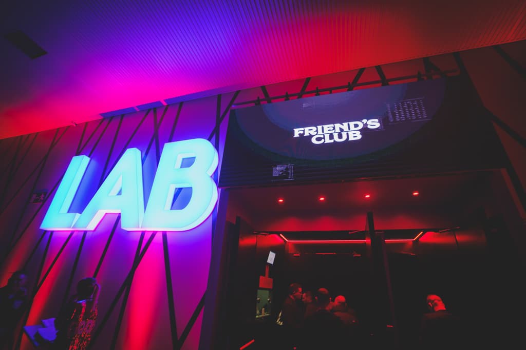 Entrada de la sala con el neón de LAB y el logo de Friend's Club